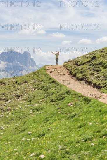Person hiking on a path with views of rocky mountains and wide skies, Schlehrn hike, Alpe di Siusi,