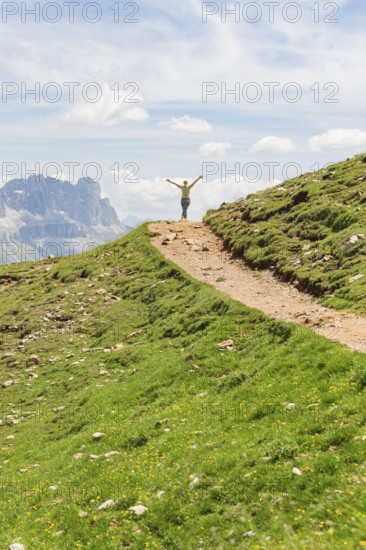 Person opens his arms on a hill path with a view of rocky mountains, Schlehrn hike, Alpe di Siusi,