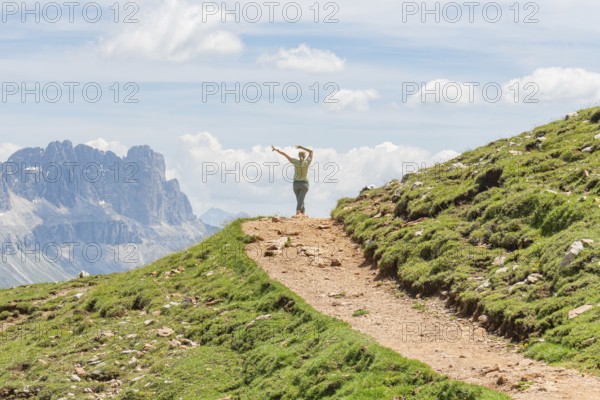 Person spreading his arms on a path in front of a majestic mountain scenery, Schlehrn hike, Alpe di