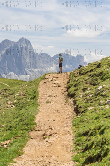Hiker standing on a path with visible rocks and imposing mountains, Schlehrn hike, Alpe di Siusi,