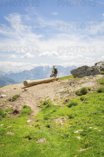A hiker sits on a tree trunk with a wide view over the mountain landscape, Schlehrn hike, Alpe di