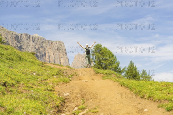 A hiker enjoys a sunny path in a mountainous landscape, Schlehrn hike, Alpe di Siusi, Dolomites,