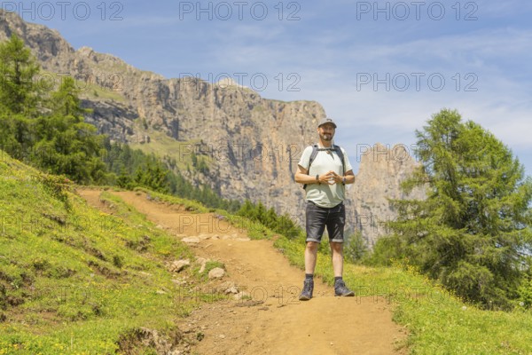 A hiker with a rucksack on a path against a rocky mountain backdrop in fine weather, Schlehrn hike,