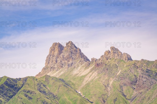 Mountain peaks rise into the sky, surrounded by green slopes and blue sky, hike to the Schlehrn,