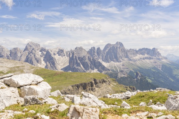 Majestic mountains under a blue sky with white clouds and green vegetation in the foreground, hike