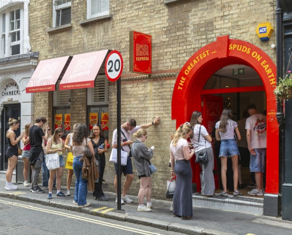 Queue line of people waiting at entrance Spud Bros Express fast-food takeaway, Soho, London,