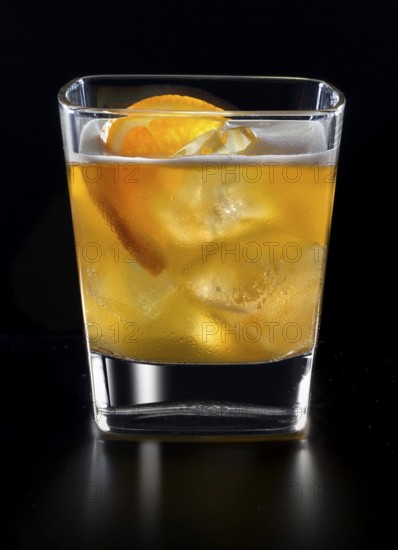 Cocktail in a tumbler on ice with half a slice of orange as garnish against a black background,