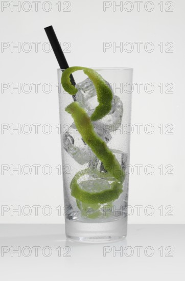 Betautes cocktail glass, filled with ice cube cubes, lime zest as garnish, in front of a white