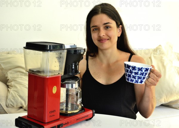 Young beautiful Southern European woman, brunette, 30 years old, demonstrating a coffee machine in