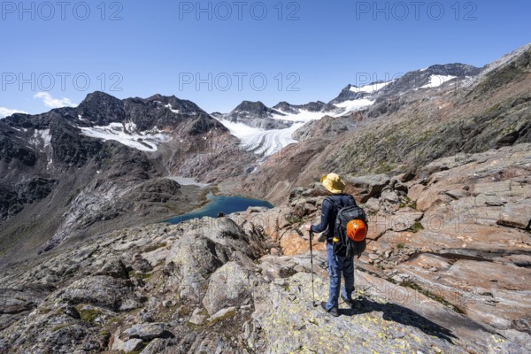 Mountaineer on hiking trail, view of blue glacial lake in rocky mountain landscape, behind