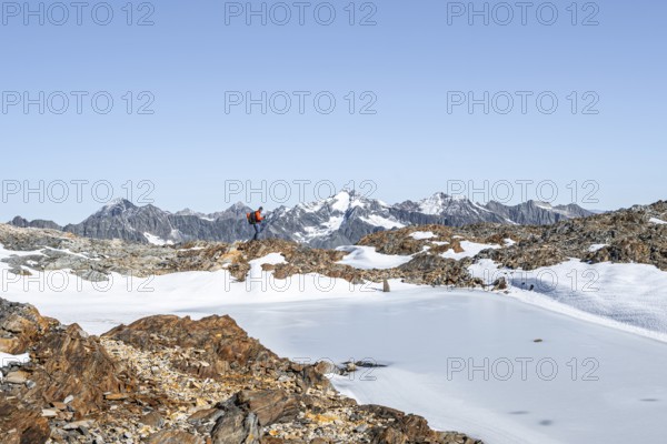 Mountaineer in rocky high mountain landscape, frozen small mountain lake, behind mountain peak