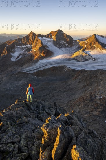 Mountaineer in front of picturesque high mountain landscape at sunrise with alpenglow, glacier and