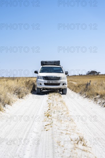 Off-road vehicle driving on a sandy track between yellow dry grass, Makgadikgadi salt pans,