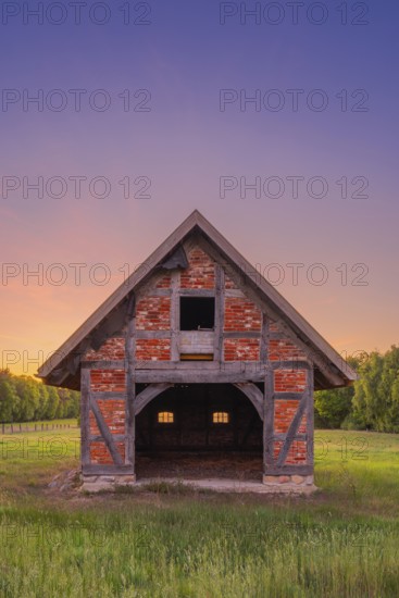 View of grasses and an open half-timbered barn standing on a pasture in the sunset, meadow, spring,