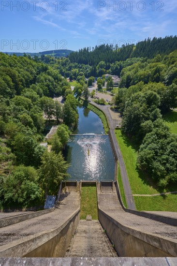 A high view of a dam with a river and lots of greenery all around under a clear sky, Oleftalsperre,