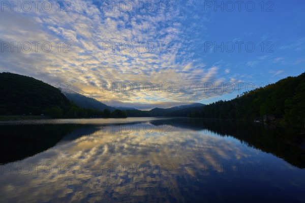 Peaceful morning atmosphere with dramatic sky reflected on the still lake, surrounded by green