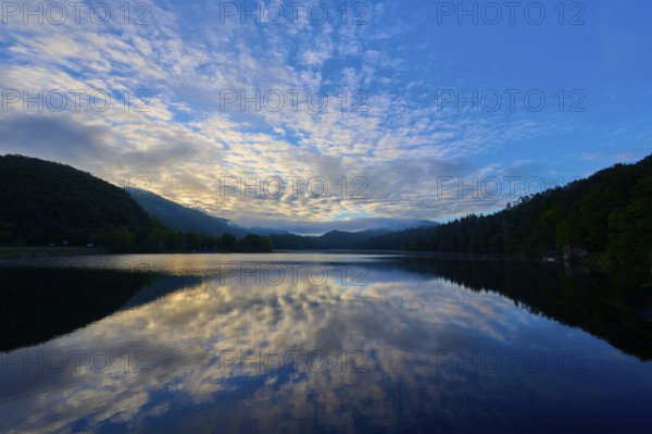 Impressive morning view with reflecting sky on a calm lake, framed by gentle mountains, summer,