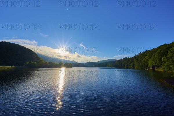 The sunny morning mood is reflected golden on the water of the lake, surrounded by peaceful hills