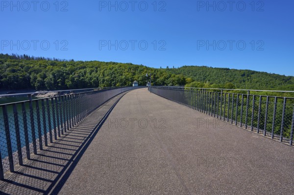 Straight view of an asphalted bridge with railing over a dam, summer, Urft dam wall, Obersee,