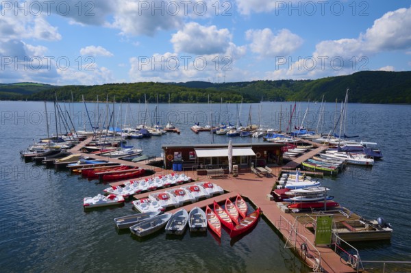 Pedal boats and other boats are moored on a jetty in a large lake and offer leisure activities,