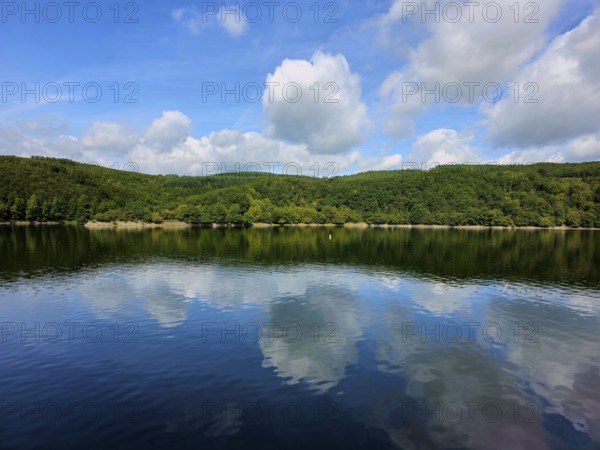Clear blue sky with white clouds reflected in the still water of a lake and wooded shores, summer,