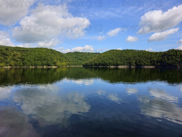 Blue sky with white clouds and their reflection in a calm lake, surrounded by lush forests, summer,