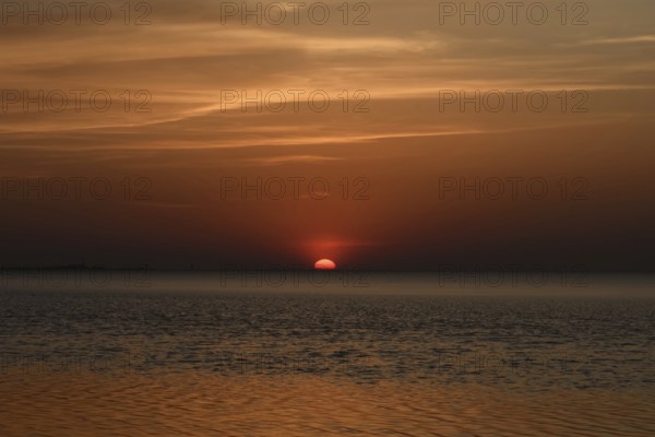 Atmospheric sunset... Cuxhaven, North Sea, in calm weather, glowing red sun sinking into the sea,