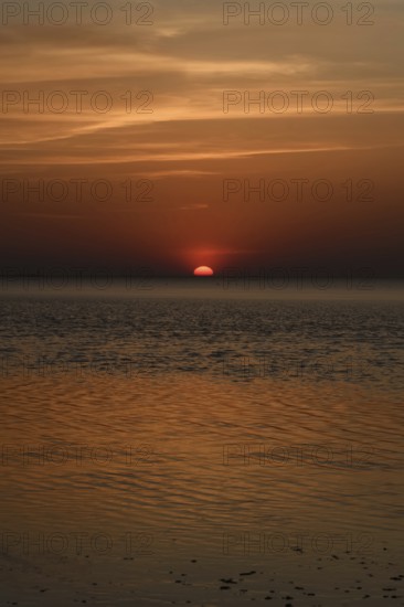 Atmospheric sunset... Cuxhaven, North Sea, in calm weather, glowing red sun sinking into the sea,