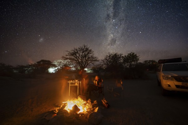Tourists sitting around a campfire next to their off-road vehicle at night, night shot with starry