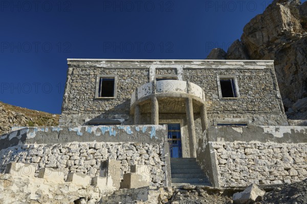 Old stone house against an imposing rocky backdrop, historic and sunlit, Embros Thermal Baths, Kos,