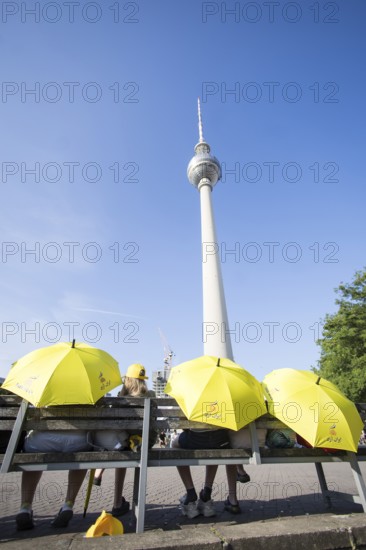 Several people sit with yellow Free Iran umbrellas in front of the television tower on