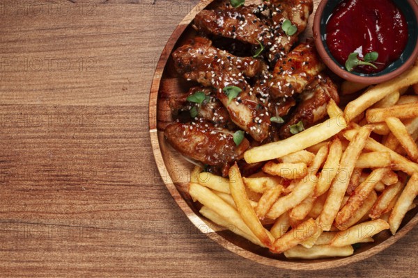Barbecue chicken wings, sprinkled with sesame seeds, with French fries, and sauce, on a wooden
