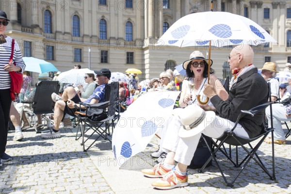 Two visitors under a parasol at the Staatsoper fÃ¼r alle, a free open-air concert with conductor