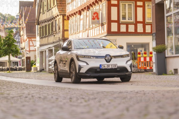 A Renault in a city street with half-timbered houses and shop windows, Deer E, car sharing,