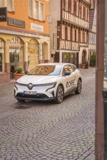 An electric car in front of half-timbered houses in a historic shopping street, Deer E, car