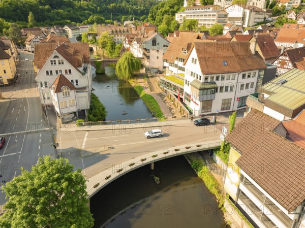 Aerial view of a town with a river and bridge, showing half-timbered buildings and green trees from