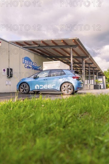 Electric car near an outdoor swimming pool, surrounded by grass and under a cloudy sky, Deer E, car
