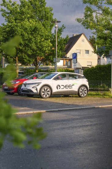 A white electric car parked in a car park in front of a house in a green residential area, Deer E,