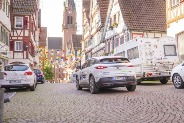 Cars parked in an old town, decorated with colourful garlands and a church in the background, Deer