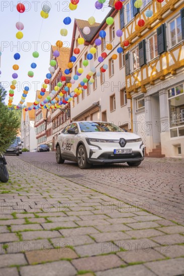 A car drives under colourful garlands in a cobbled street, Deer E, car sharing, electric car, Calw,