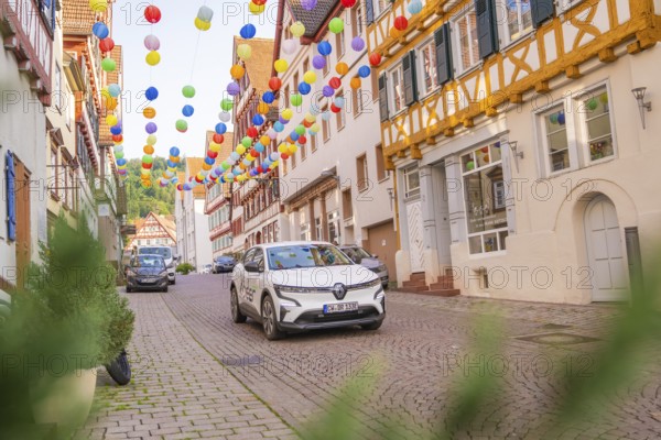 A car drives through a street decorated with colourful garlands in an old town, Deer E, car