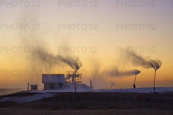 Snow cannons blow clouds of smoke on a hilltop under the purple twilight sky, winter, Route de