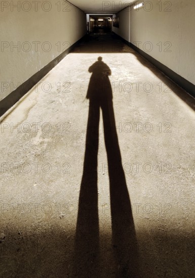 Long shadow of a person in the tunnel of the underpass to the railway tracks, train station, Bad