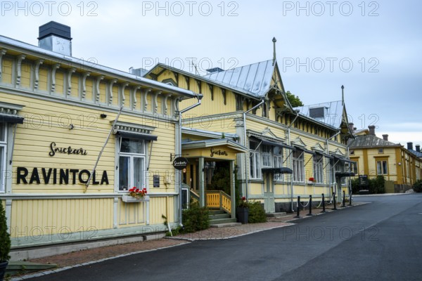 Yellow restaurant building with decorative wooden design, located on a quiet street, conveys