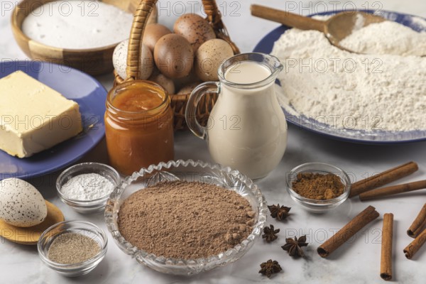 Baking ingredients, flour, sugar, cinnamon, milk, butter, cocoa, jam and eggs on a table
