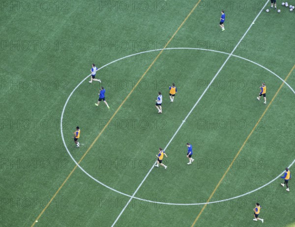 Players wearing colorful jerseys play soccer on a grass field from a bird's eye view from the tower