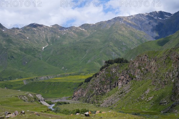 View of a green valley with a river surrounded by rocky and grassy mountains, Terek River, Kazbegi,