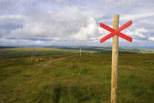 Red snowmobile snowscooter marker on a wooden post in front of a vast landscape under clouds,