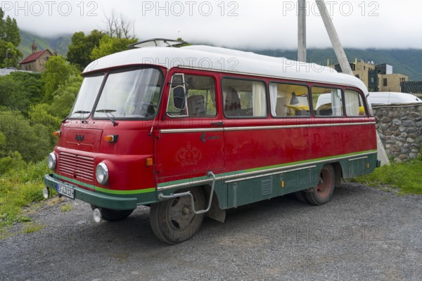 Red retro bus with green stripes on a road in a rural mountain landscape, vintage car, Robor LO