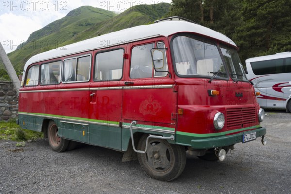 Old nostalgic bus in red with green accent on a parking lot in a mountainous landscape, vintage